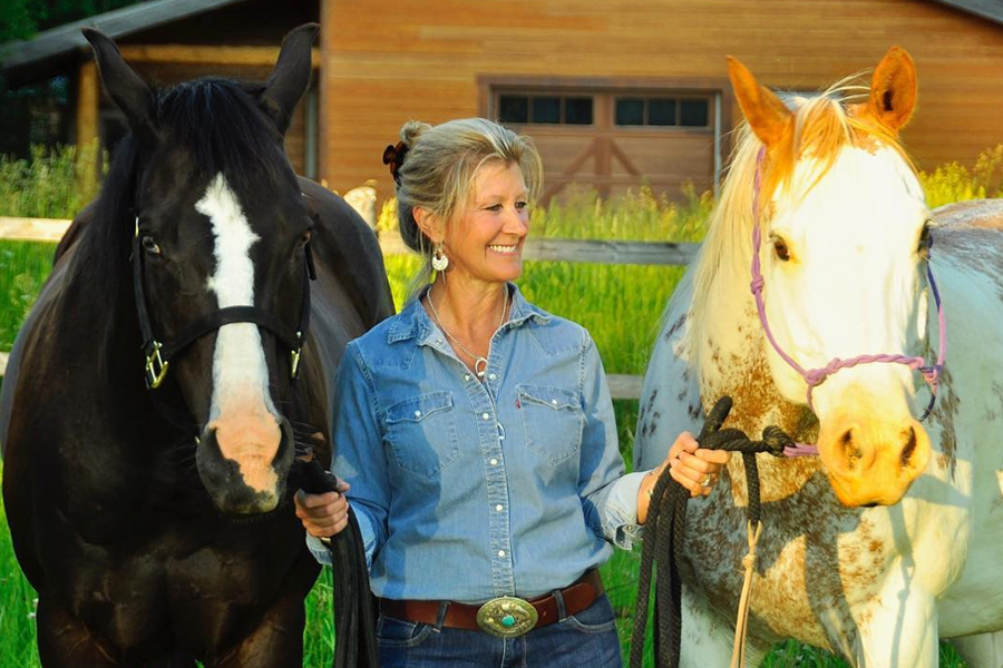 Deb Cerbone leading an appaloosa horse and a black horse with blaze