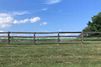 Three board wood fencing with grass and sky