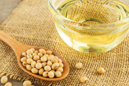 oil in a small bowl next to a wooden spoon holding raw soybeans
