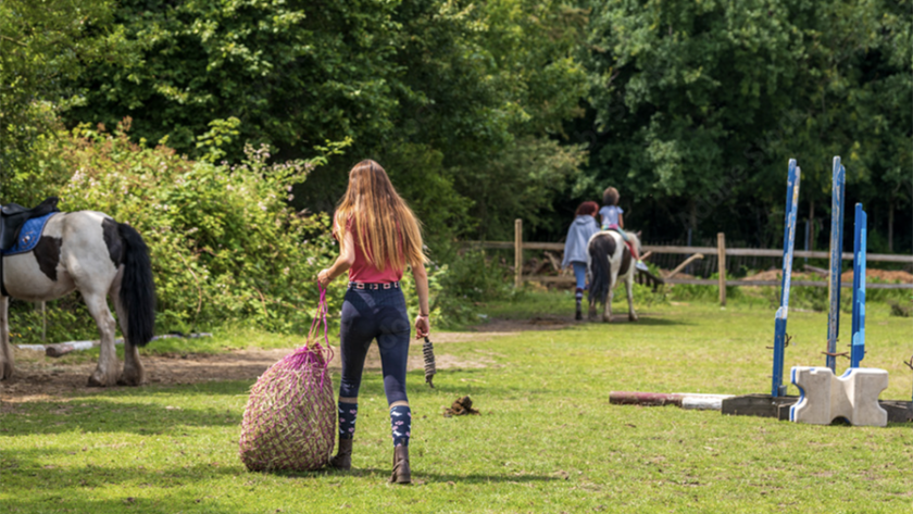 Girl carrying a haynet at a horse farm