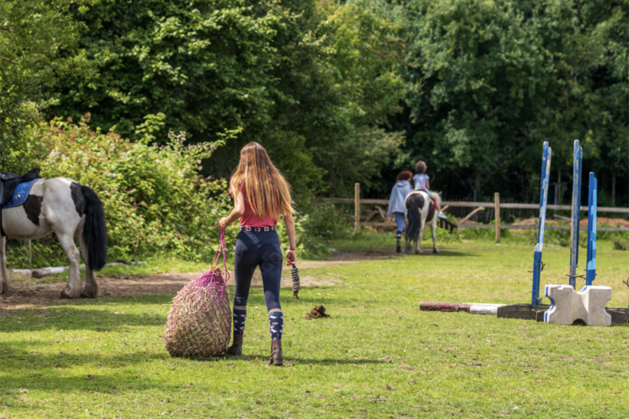 Girl carrying a haynet at a horse farm